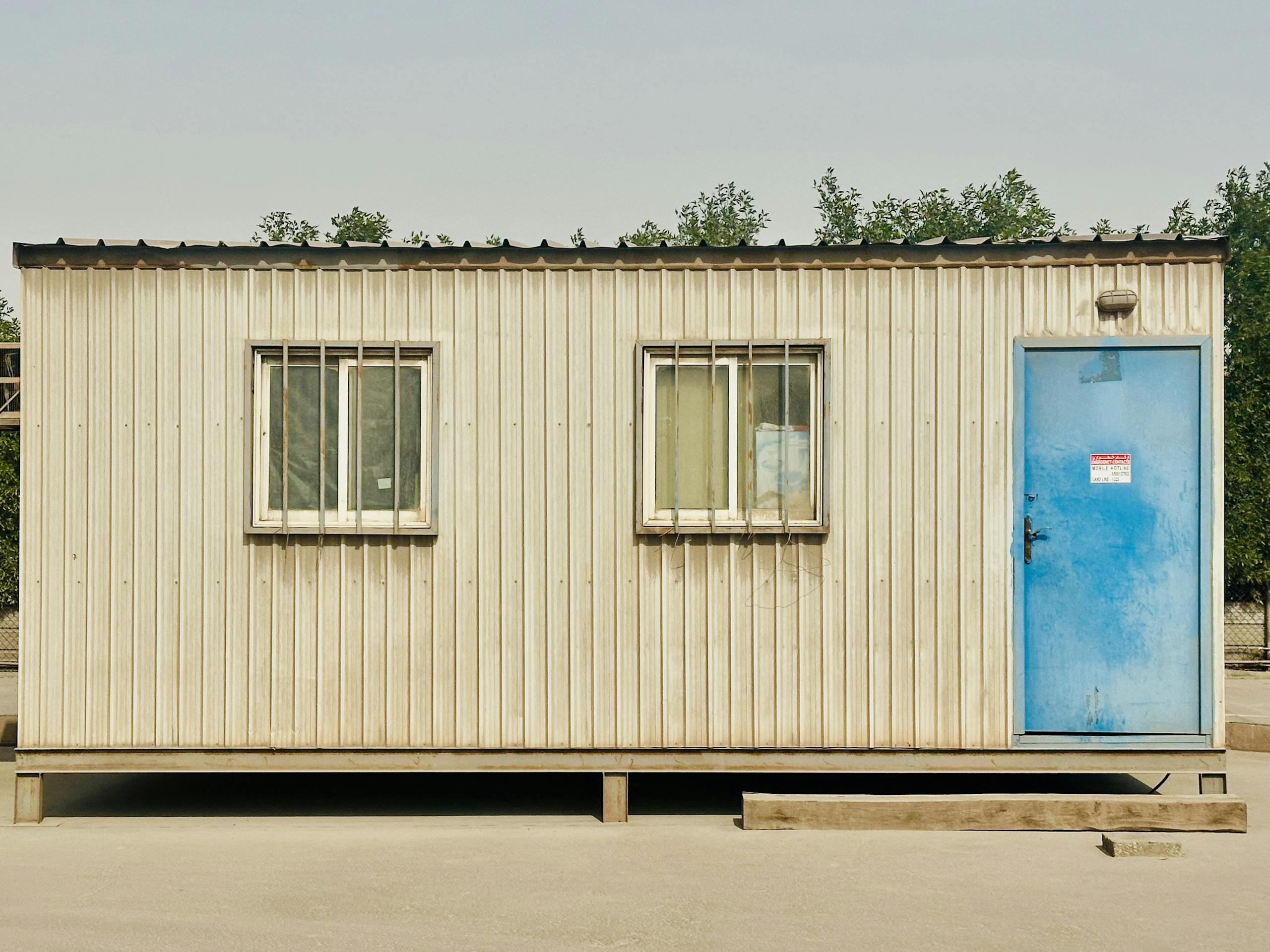 A portable cabin with a distinctive blue door in a sunny outdoor setting in Saudi Arabia.