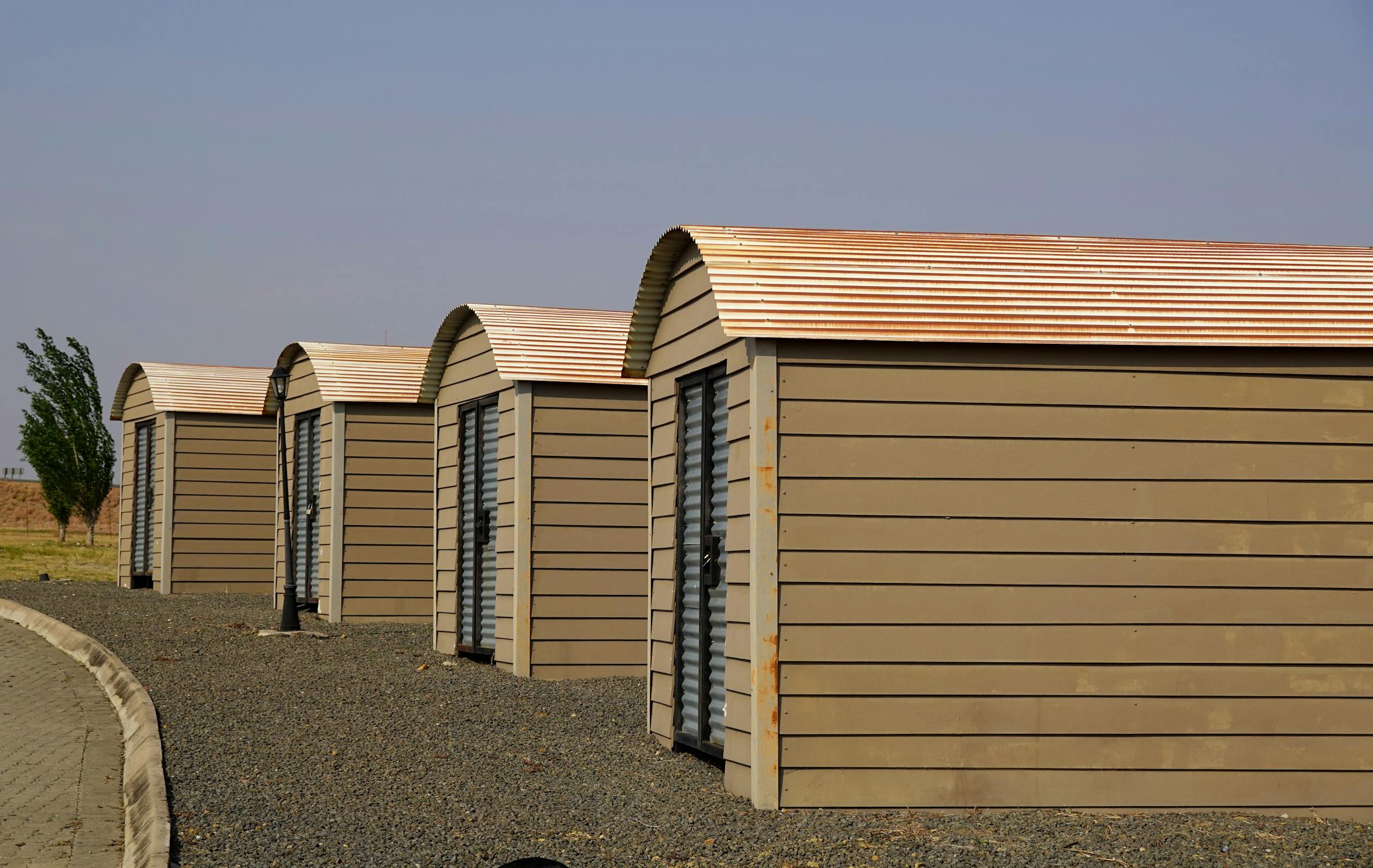 Four identical modern storage sheds aligned on a gravel surface with clear skies.